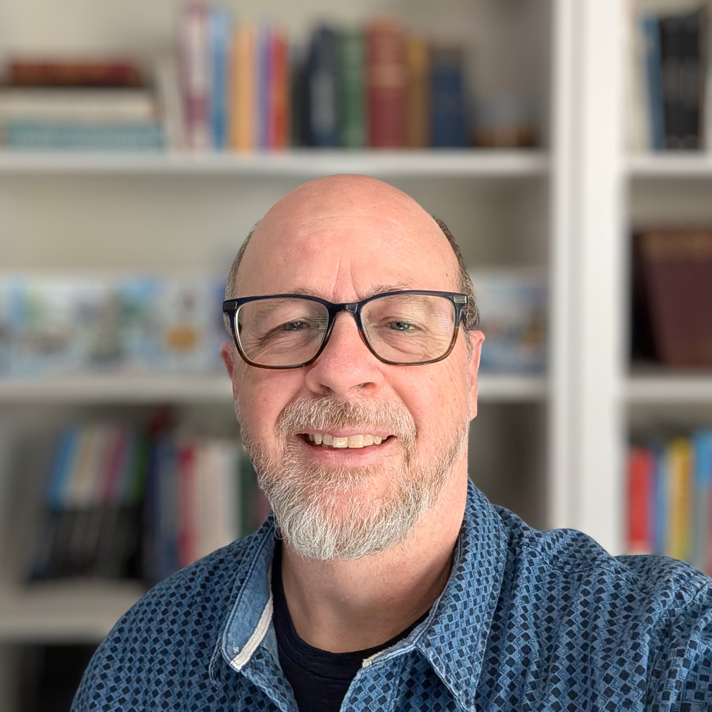 Gary Stream, smiling in glasses and a blue patterned shirt, in front of shelves of books.